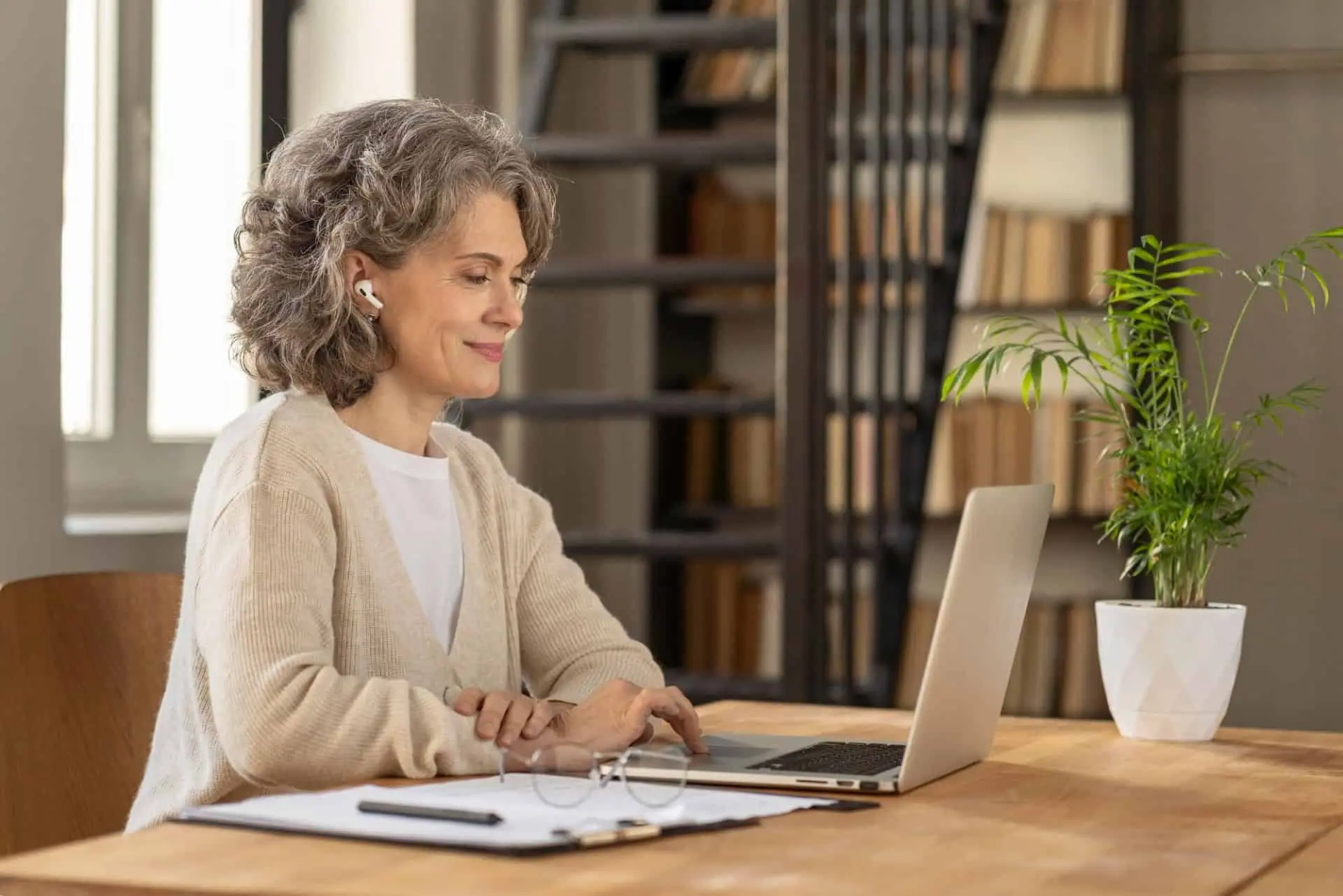 An older woman working on a laptop at a wooden desk