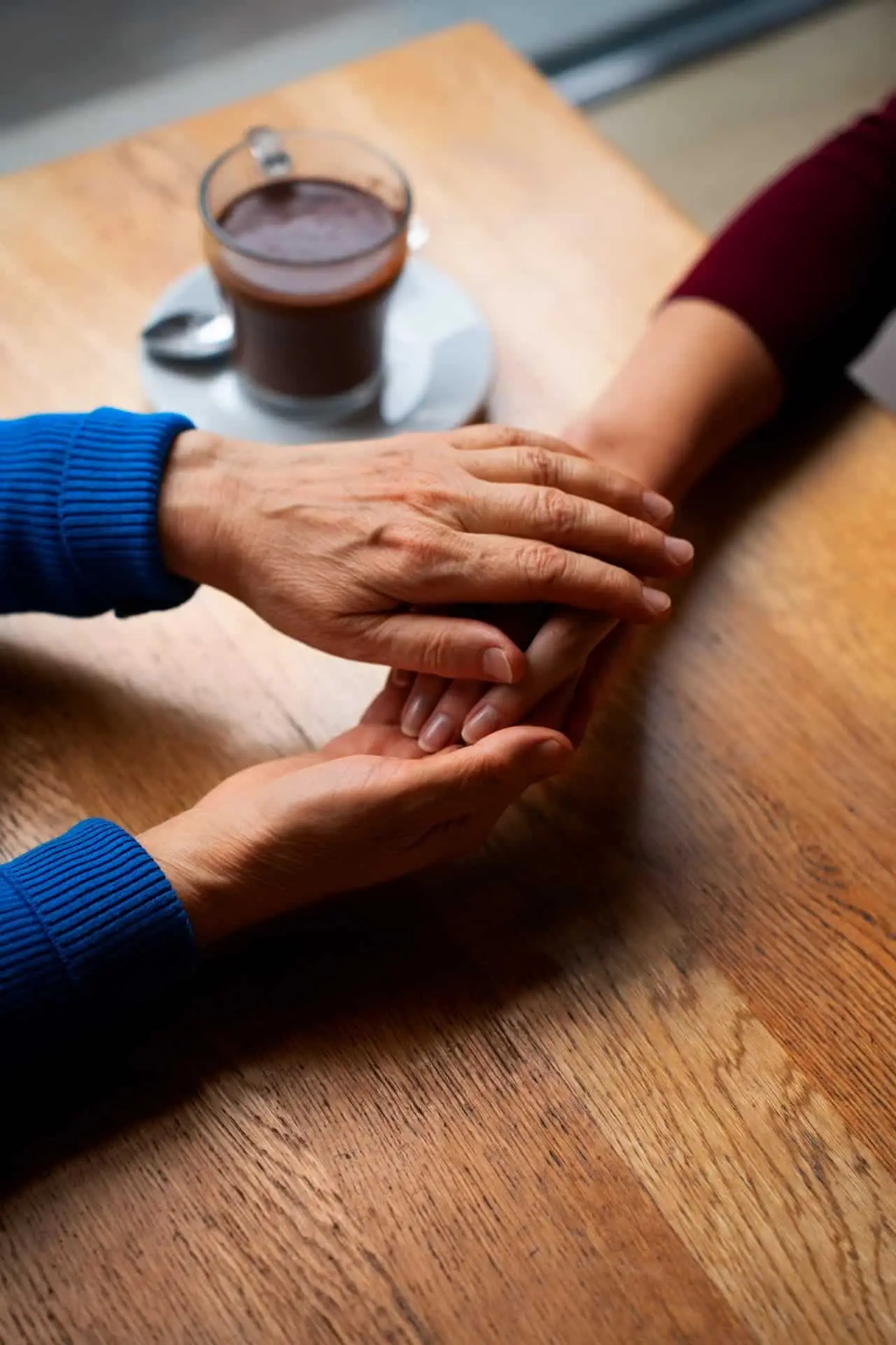 Two people holding hands across a wooden table